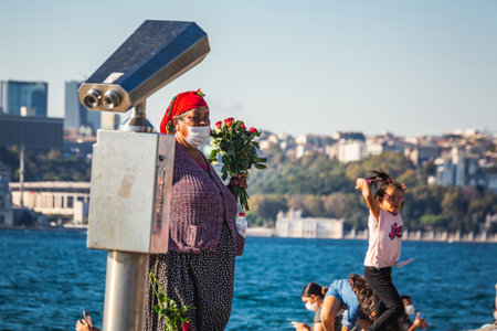 Woman cells roses near Maiden's Tower. IT is a tower lying on a small islet located at the southern entrance of the Bosphorus in Istanbul, Turkey. Istanbul, Turkey - October 01 2020.のeditorial素材