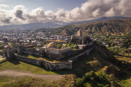 Aerial view of a historic Rabati fortress with stone walls and towers, set against a backdrop of a modern town and rolling hills under dramatic cloud formations.の写真素材
