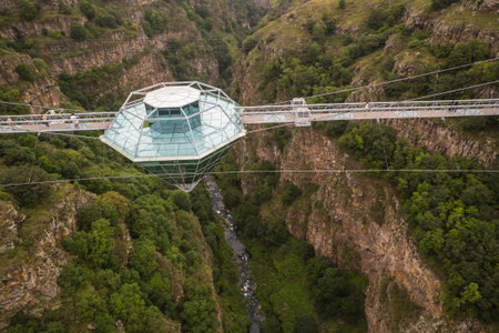 A stunning aerial view of a glass Diamond Bridge, suspended over a deep canyon, surrounded by rugged...