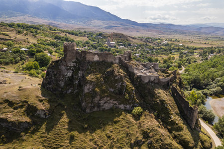 A striking aerial view of a Atskuri fortress perched on a cliff, with rugged rocky terrain and mountains in the background under a partly cloudy sky.の写真素材