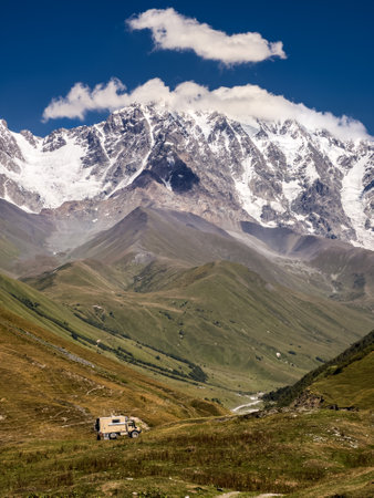 Valley with motorhome and a stunning backdrop of snow-capped mountains and lush hills in Georgias...