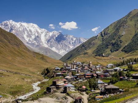 Picturesque view of Ushguli village nestled in the valley with medieval stone towers and a stunning backdrop of snow-capped mountains and lush hills in Georgias Caucasus region.の写真素材