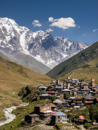 Picturesque view of Ushguli village nestled in the valley with medieval stone towers and a stunning backdrop of snow-capped mountains and lush hills in Georgias Caucasus region.の写真素材