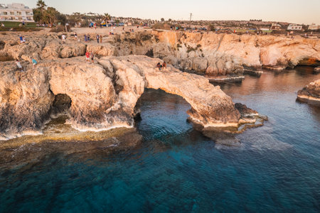 A breathtaking view of a natural rock arch over the sea, with a glowing sunset reflecting on the calm waters.の写真素材
