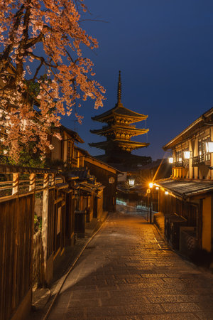 Night view of Yasaka Pagoda in Kyoto, Japan, illuminated under a twilight sky. Cherry blossoms frame the scene, adding a touch of springtime elegance to this ancient Japanese street.の写真素材