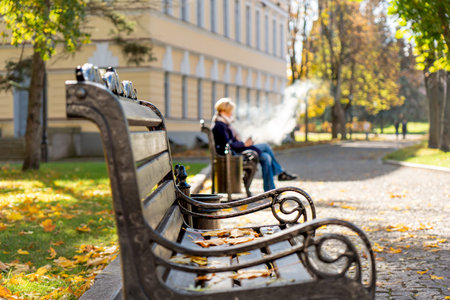Old woman sitting on a bench in the autumn park and smoking cigaretteの写真素材
