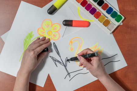 Female hands drawing a flower with paints on a white sheet of paperの写真素材