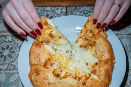Close-up of a woman's hands with a red manicure holding a piece of cheese pie.の写真素材