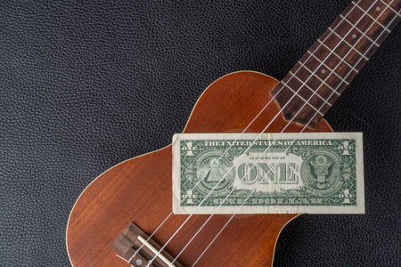 Ukulele and one dollar banknote on a black leather background