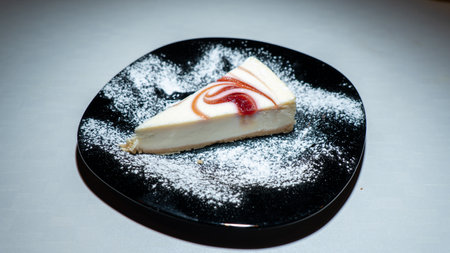 Piece of cheesecake on a black plate with sugar powder.の写真素材