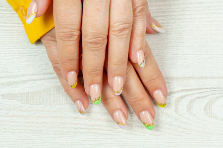 French manicure in green, yellow, purple on a solid background. Nail art on women's nails. Women's hands with manicure.の写真素材