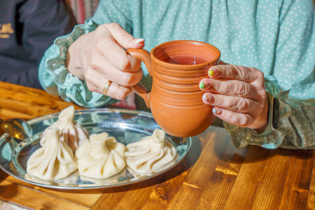 Woman's hands hold a clay cup with hot tea and dumplingsの写真素材