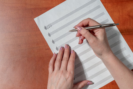 Woman's hands holding a pen and writing on a sheet of musicの写真素材