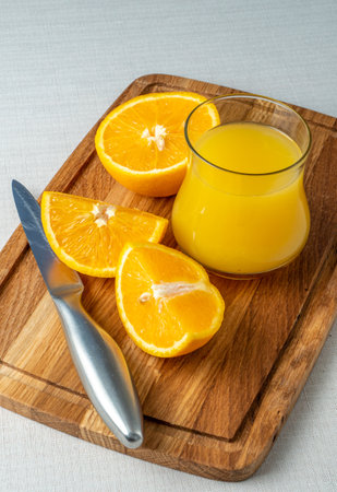 Orange juice in glass and sliced orange on wooden cutting board with knifeの写真素材