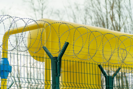 Barbed wire on the fence, a fence made of steel grating. Spiral barbed wire with sharp steel spikes on top of a perimeter fence made of wire meshの写真素材