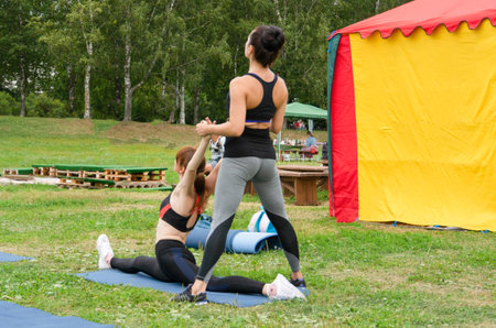 Two girls are engaged in yoga on the grass in the park.の写真素材