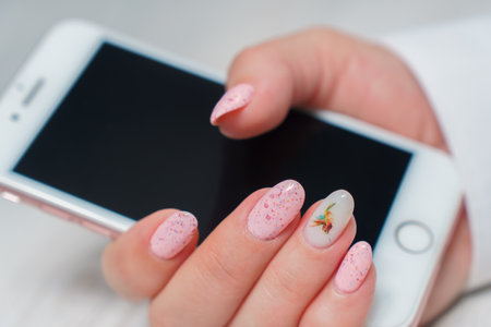 Female hands with pink nail design. Glitter pink nail polish manicure. woman holding smartphone.の写真素材