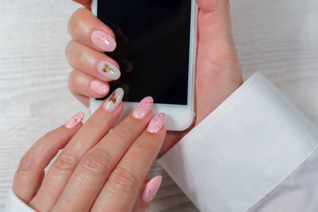 Female hands with pink manicure and mobile phone on a white background.の写真素材