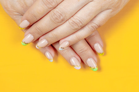 Female hands with beige and green manicure on yellow background.