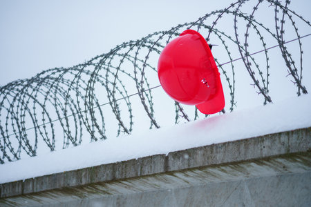 Red helmet and barbed wire on a fence in the snow.の写真素材