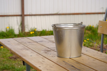 Metal bucket on a wooden table in the garden, front view.の写真素材