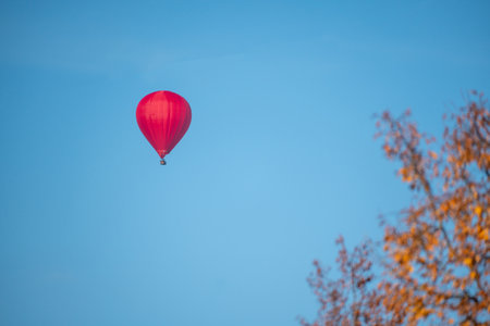Red hot air balloon flying in the blue sky over autumn trees.の写真素材