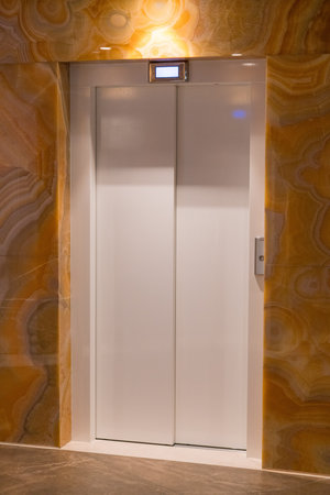Closed elevator doors in modern lobby with marble wall and warm lighting. Interior of hotel or...