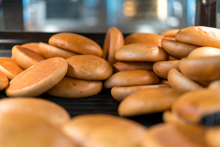 Freshly baked burger buns on bakery conveyor or rack industrial bread production food factory...