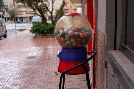 Colorful gumball vending machine filled with toy capsules standing outside store on city sidewalk.の写真素材