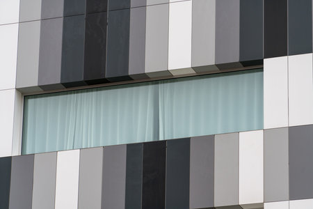 Contemporary architectural facade with geometric panels and wide horizontal window with curtains.