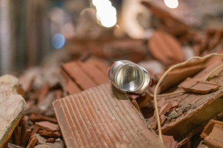 Small flashlight lying on broken roof tiles and construction rubble. Close up with shallow depth of...