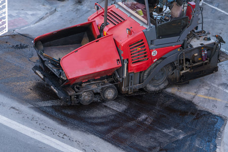 Road construction machine laying fresh asphalt on urban street surface. Asphalt paver equipment used for road repair and infrastructure maintenance.の写真素材