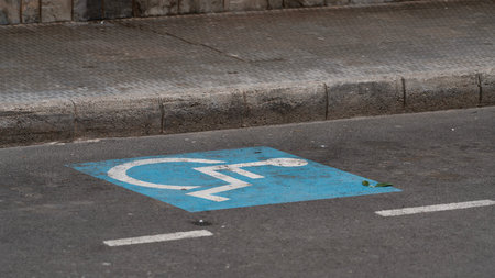 Accessible parking space symbol painted on asphalt near sidewalk. Urban infrastructure for...