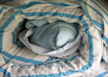 Roll of dirty bedclothes convolute, in centre green pillowの写真素材