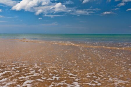 A tropical beach with gentle waves in the sky with cloudsの写真素材