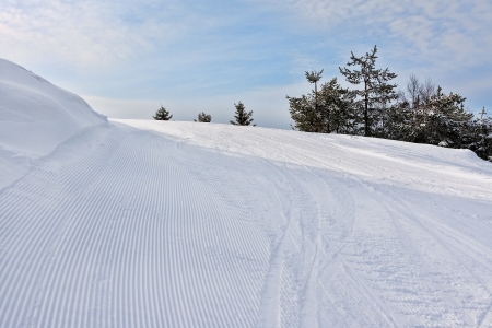 View on empty fresh-made downhill ski slope and mountains on a sunny dayの写真素材