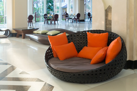 Wicker sofa with orange pillows in the lounge.のeditorial素材