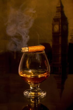 a glass of whiskey and a cigar on the tableの写真素材