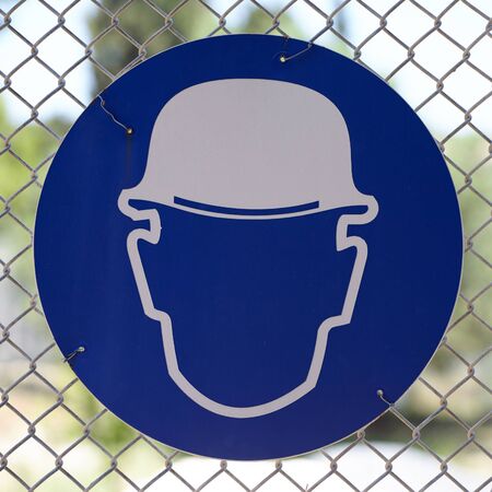 The blue sign of wear safety helmet symbol in front of the construction site