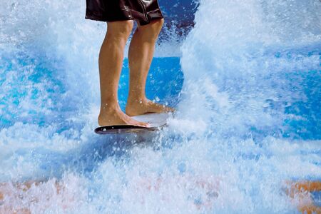 Man take wake surf, riding a surfboard or foot board along an outdoor water slide set up