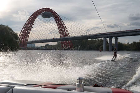 Moscow, Russia - September 28, 2008: Wakeboarding rider showing tricks and skills at free ride on the city river near cable-stayed bridge. Wakeboarder behind the motorboatのeditorial素材