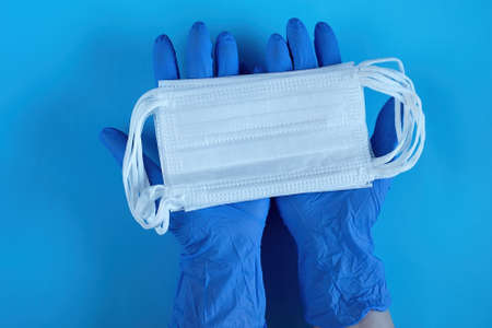 Two hands of a Doctor in medical gloves holds, takes, gives medical surgical masks for covering the...