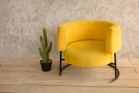 The interior of the room with a yellow chair, on the wall with decorative plaster, wooden floor, cactus in a pot near the chairの写真素材
