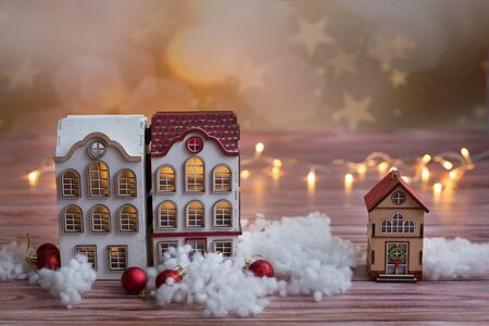 Beautiful toy wooden houses on a snowy background, Christmas toys, on a wooden background with garlandsの写真素材