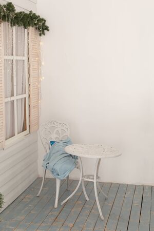 A white table with a chair stands on the terrace by the garland windowの写真素材