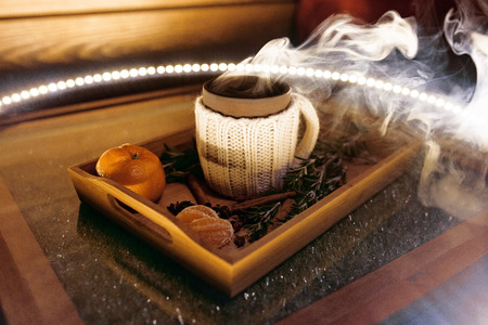 A mug of warm tea with pieces of manadarines on a wooden tray in the smoke in a cafeの写真素材
