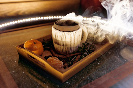A mug of warm tea with pieces of manadarines on a wooden tray in the smoke in a cafeの写真素材