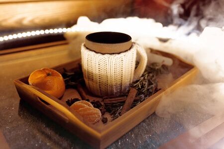 A mug of warm tea with pieces of manadarines on a wooden tray in the smoke in a cafeの写真素材