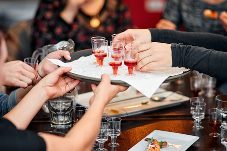 Small glass glasses of alcohol on a tray held by several people in a restaurant