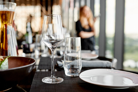 Empty glass goblets on the table  and white table setting with a jar of juice and aa girl on the background in the restaurantの写真素材
